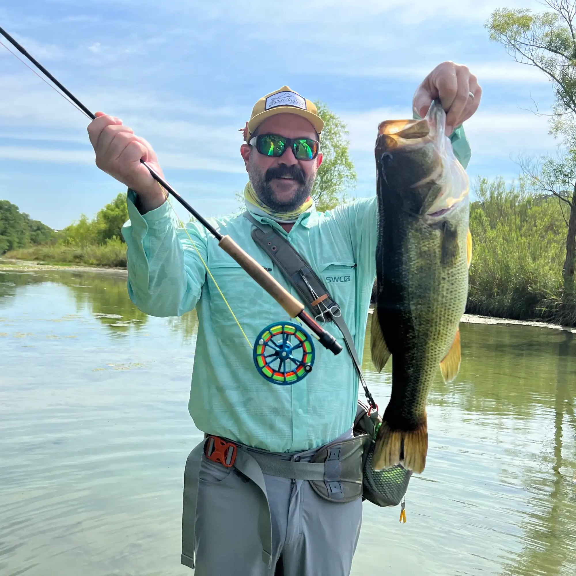 Man holding a large largemouth bass with a thomas and thomas fly rod and a Ross reel